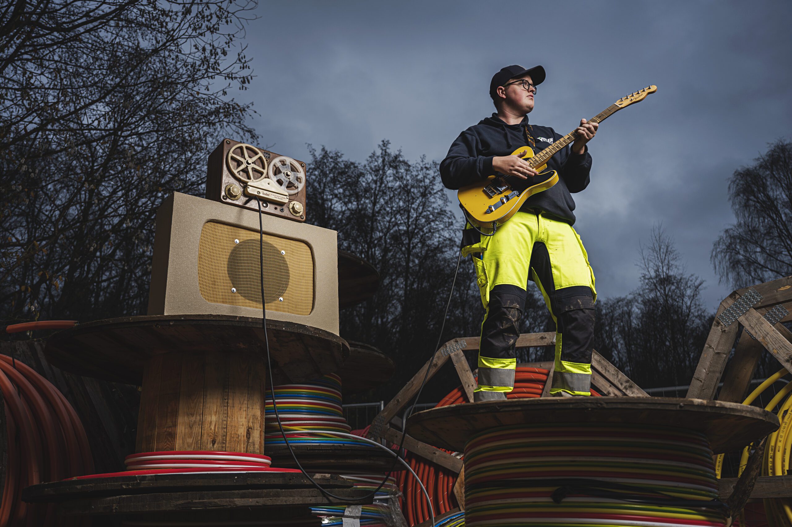Bildet viser en mann som står på en kabeltrommel og spiller elgitar